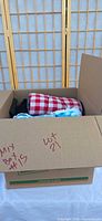 Box containing plaid picnic blanket and blue fleece throw