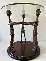 Full view of table showing glass top, three embracing metal figures, and wood base