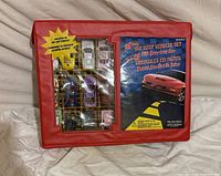 Front of closed red carry case showing clear window with cars displayed and printed insert