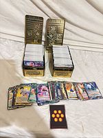 Two open gold Yu-Gi-Oh tins filled with stacked Dragon Ball Super cards and a spread of loose cards in front