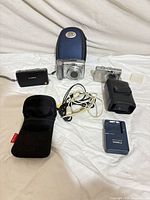 All three cameras, charger, cases, pouch, cables displayed on white background