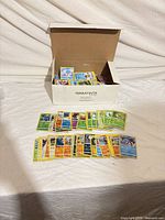 Open cardboard box labeled TERRATINTA containing stacked Pokémon cards with additional spread of cards in front