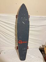 Top of longboard showing grip tape, Quest logo, pintail shape