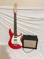 Guitar standing upright next to amplifier with cable visible