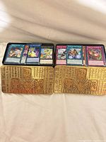 Two gold embossed tins with visible Yu-Gi-Oh! cards displayed on top