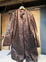 Front view of brown leather coat on hanger showing full length and sleeve condition