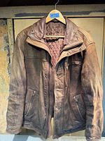 Front view of brown leather jacket on hanger showing quilted lining, zipper, pockets