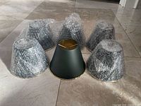 Six dark green metal chandelier bulb shades, five wrapped in bubble wrap, one unwrapped showing gold interior