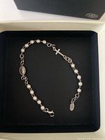 Bracelet laid in box showing bead links, cross charm, lobster clasp, oval tag, and packaging
