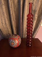 Tall dark pink glass bottle vase and spherical patterned candle side by side