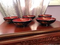 All five bowls displayed on wooden surface showing black exterior with red interior