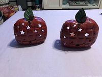 Front view of two red metal apple-shaped tealight holders showing star cutouts and green leaves
