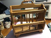 Front view of oak magazine rack showing handle, slatted dividers, raised feet