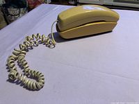 Side view of yellow Radio Shack trimline phone on surface showing handset resting on base and coiled cord