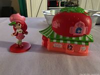 Strawberry Shortcake figurine and strawberry house toppers side by side