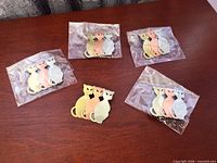 Five individually bagged trio cat pins on table
