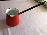 Side view of red enamel syrup pot with long black handle
