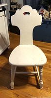 Front view of white wooden chair showing shaped backrest, curved seat, turned front legs