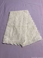 Folded white eyelet table runner showing overall size and scalloped edge
