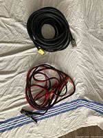 Coiled black extension cord and red/black jumper cables laid on cloth background