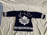 Front view of navy and white hand-knitted Toronto Maple Leafs youth sweater laid flat on bed