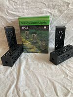 Box displaying Solar Garden Lights 8PCS and three light housings for scale