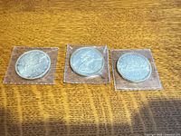 Three 1966 Canadian silver dollars in flips on wood surface