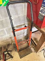 Full view of red and black steel hand truck against wall