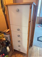 Full view of tall pine-framed cabinet with white front and grey knobs