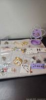 Overview of all 13 earring pairs and purple stand displayed on mat