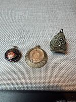 Three pendants laid out: cloisonné, coin, pyramid