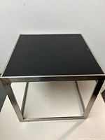 Full view of square end table showing black glass top and metal frame