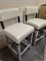 Two white bycast leather counter stools with black legs, still partly wrapped