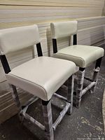 Front view of two white counter stools with black legs