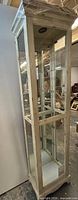 Full view of tall weathered white curio cabinet with glass panels