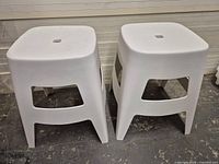 Front view of both white plastic stools showing square tops and side cutouts