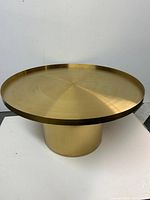 full view of round gold metal coffee table showing top and pedestal base