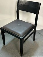 Full view of black wood chair with brown padded seat