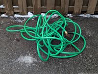 Coiled green garden hoses on pavement showing overall appearance and brass fitting