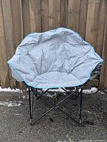Front view of grey saucer-style folding camping chair showing fabric seat, blue trim, steel frame and cup holder