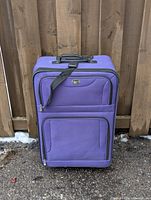 Front view of purple suitcase showing zippered compartments and wheels