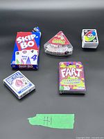 All five games arranged: Skip-Bo box, Pizza Party slice case with dice, UNO All Wild deck, Fart boxed game, Bicycle deck