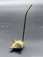 Side view of brass mouse candle snuffer on black background.