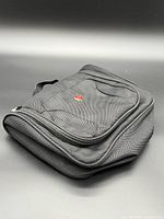 Angled view of black Swiss Gear travel pouch showing red logo, zippers, handle