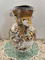 Full view of glass vase filled with mixed jewelry pieces