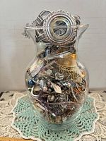 Glass vase filled with assorted jewelry; cuff bracelet visible at top
