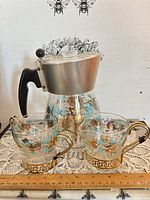 Front view of glass coffee carafe, creamer and sugar bowl showing pinecone motif and ruler for scale