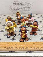 Group shot of all seven painted clay figurines beside ruler for scale