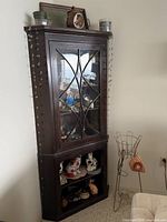 Full view of dark wood corner cabinet with glass astragal door and lower open shelves