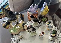 Overview of nine ceramic bird and duck figurines displayed on lace doily